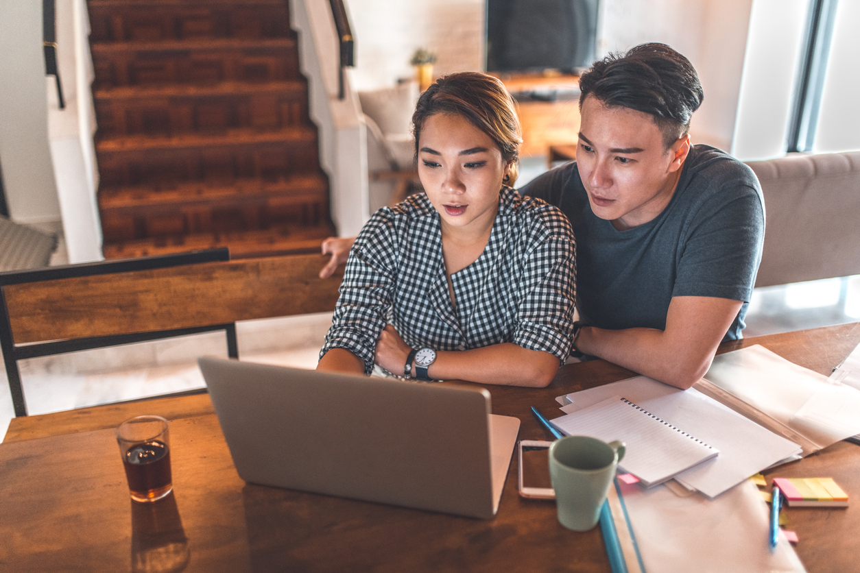 A young couple checking their information, using a laptop and surrounded by papers