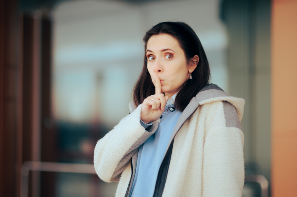 Woman in winter coat with finger over her lips.
